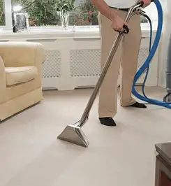 Professional carpet cleaner using a hot-water extraction wand and hose machine in a living room in El Paso, TX.