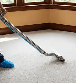 Steam carpet cleaning technician using a hot-water extraction wand on a residential carpet, wearing blue protective shoe covers El Paso, TX.