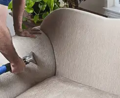 Professional upholstery cleaner deep-cleaning a fabric sofa with a handheld extraction tool and hose in El Paso, TX.